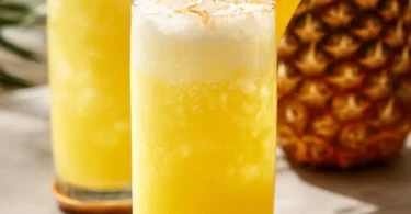 Erfrischende Ananaslimonade in einem Glas mit frischen Ananasstücken.