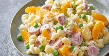 Nudelsalat mit Mandarinen und frischen Zutaten auf einem Tisch angerichtet.