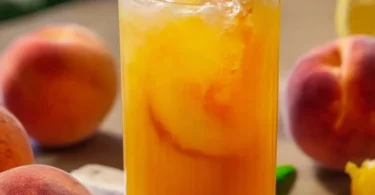 Erfrischende Pfirsich-Limonade in einem Glas mit frischen Pfirsichen und Eiswürfeln