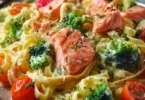 Cremige Pasta mit Lachs, Brokkoli und Tomaten auf einem Teller serviert.