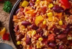 One-Pan Rice mit Paprika, Bohnen und Mais auf einem Holzbrett serviert.