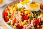 Thunfisch-Salat mit Eiern, Mais und Paprika auf einem Teller serviert.